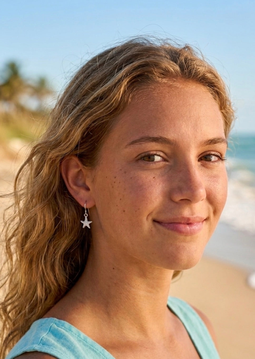 A woman wearing a small silver starfish shaped dangle earring.
