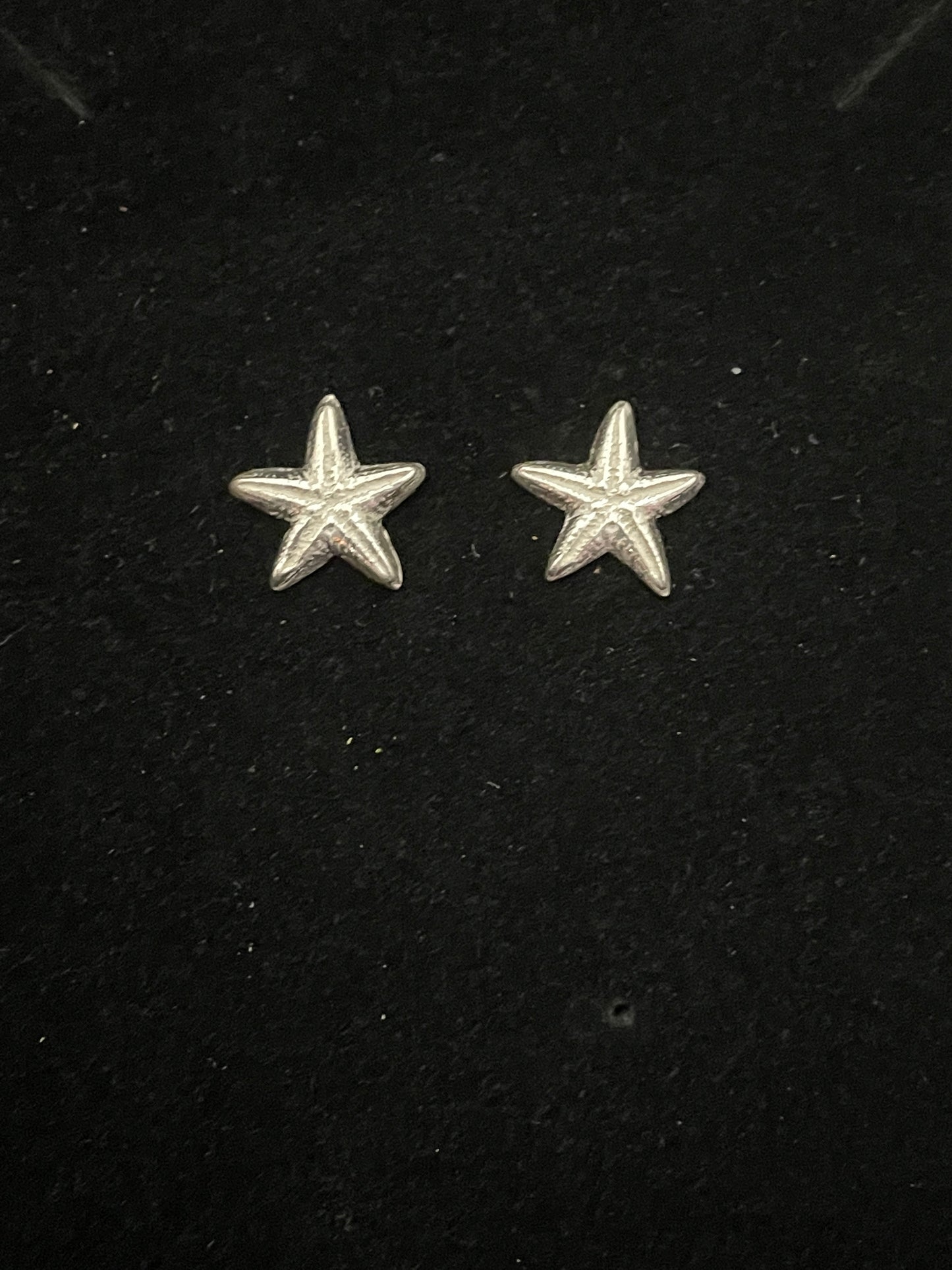 Small detailed silver starfish stud earrings on a black background
