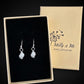A pair of silver dangle earrings displayed in an open black-lined jewelry box, with the branded Molly and Me Jewellery outer box behind it on a black background.
