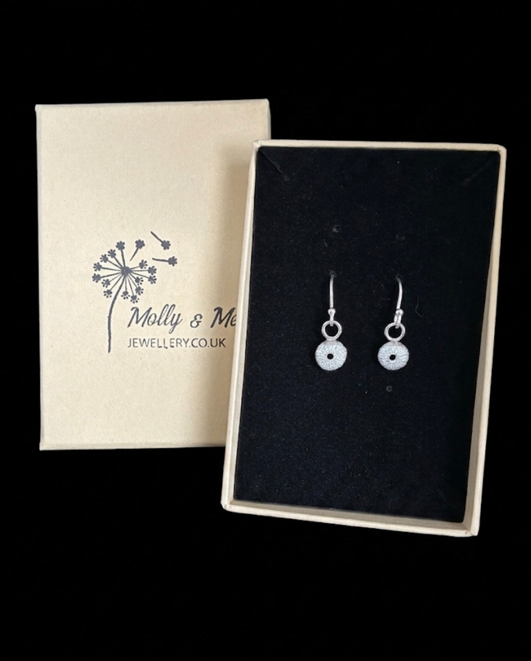 Pair of silver earrings with small sea urchins dangling from ear wires set in black velvet next to a Molly and Me Jewellery branded box. 