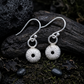 Pair of silver dangle earrings with sea urchin shell charms set on a dark natural background 