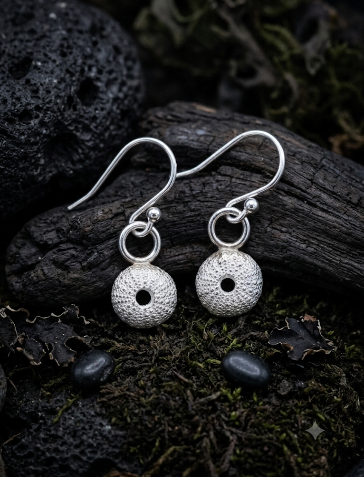 Pair of silver dangle earrings with sea urchin shell charms set on a dark natural background 