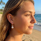 A woman in profile at a beach wearing a delicate silver drop earring with a sea urchin charm. 