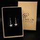 Silver starfish dangle earrings with detailed surface displayed in an open black-lined gift box next to its kraft paper packaging box branded 'Molly & Me Jewellery’. 