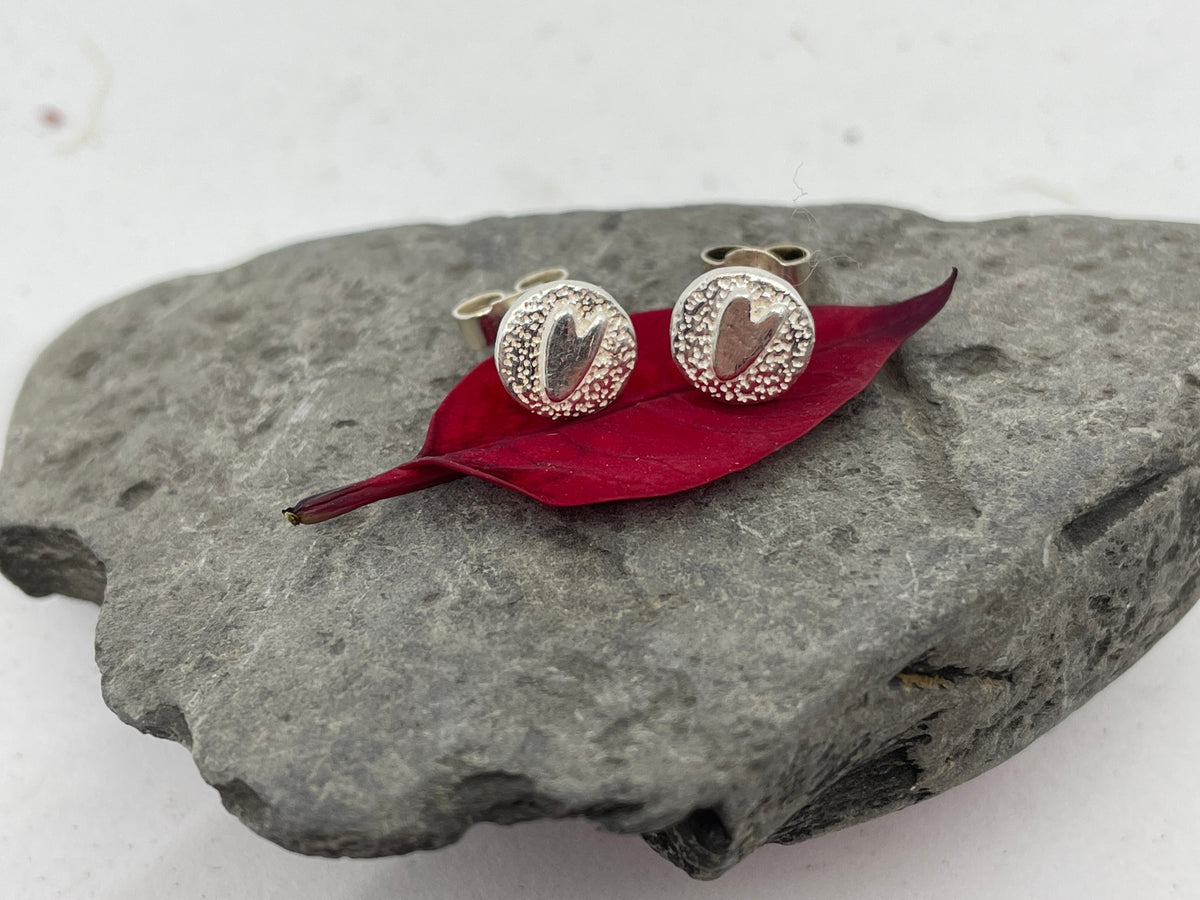 Textured disc shaped stud earrings with tiny smooth hearts set on a red leaf for love 