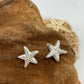 Small handmade fine silver starfish stud earrings set on a tn coloured background 