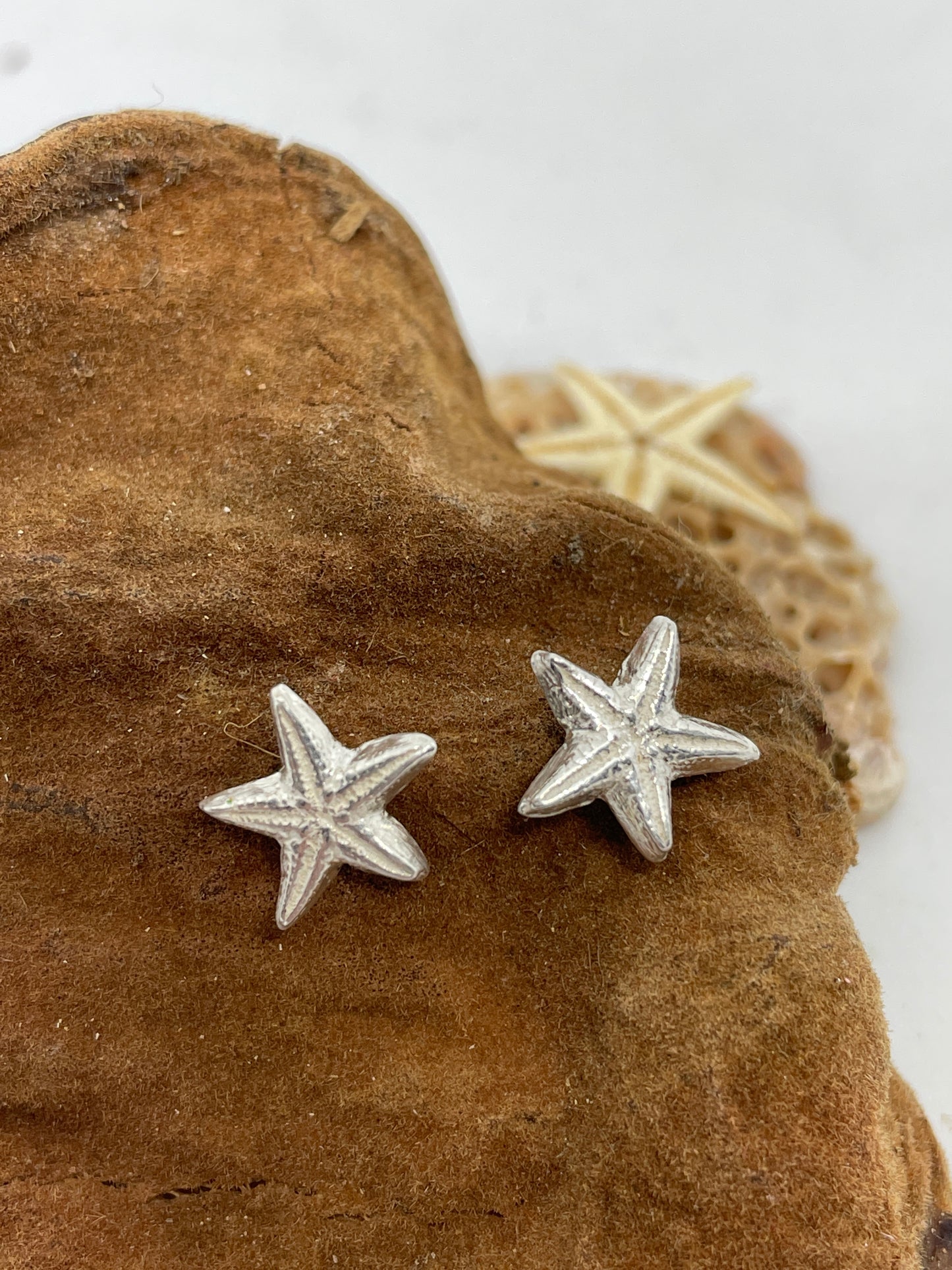 Small handmade fine silver starfish stud earrings set on a tn coloured background 