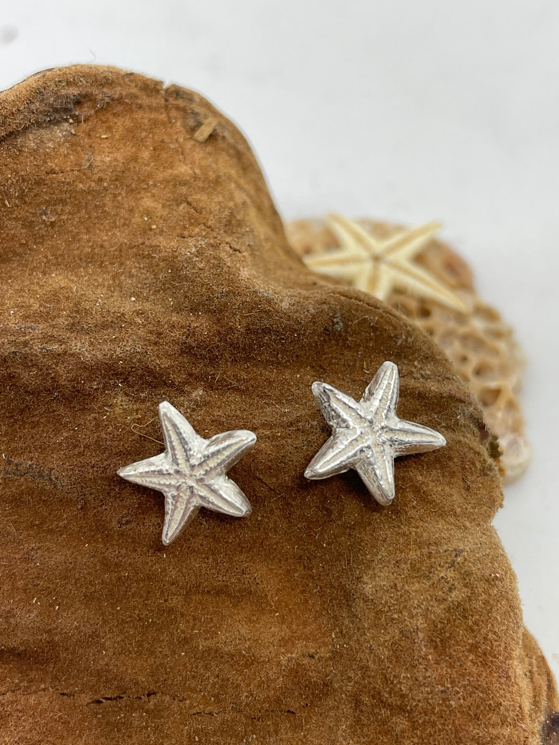 Small handmade fine silver starfish stud earrings set on a tn coloured background 