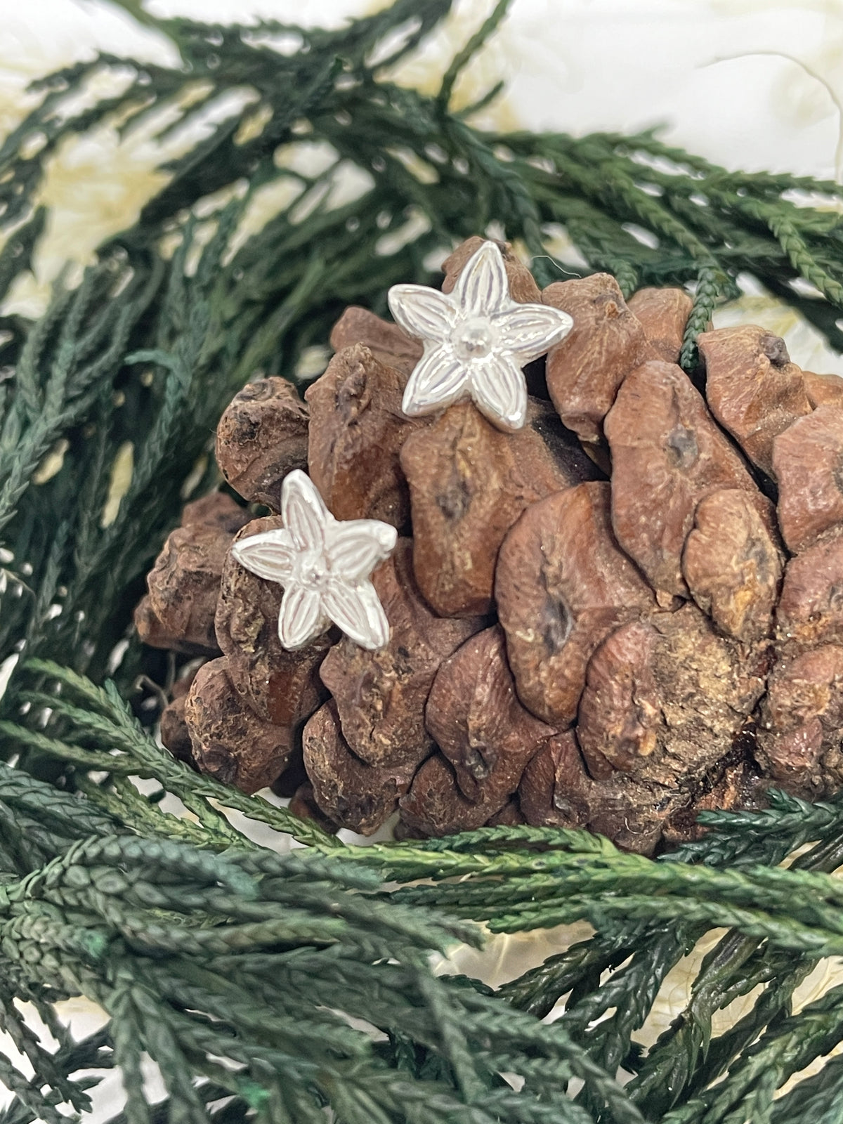 Tiny silver handmade flower stud earrings set on a pine cone