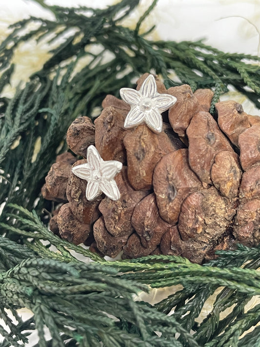 Tiny silver handmade flower stud earrings set on a pine cone