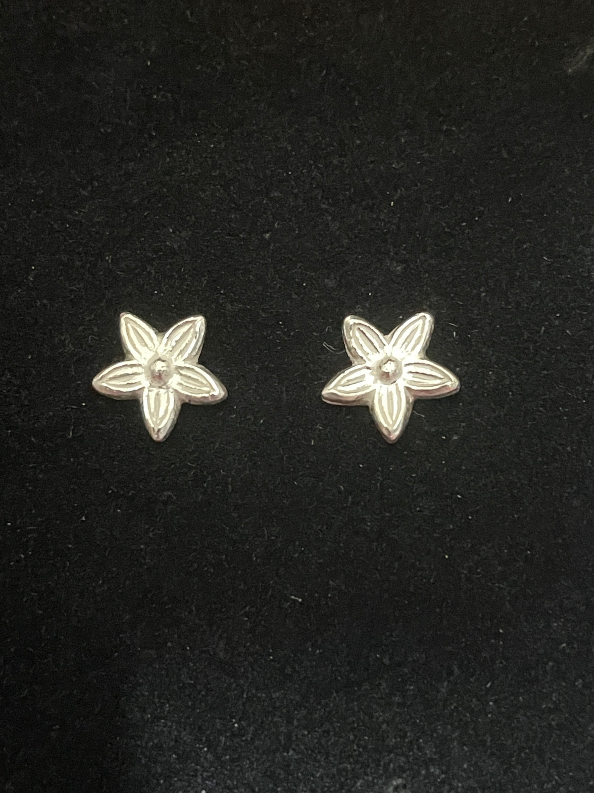 Close up of tiny silver flower stud earrings on a black background